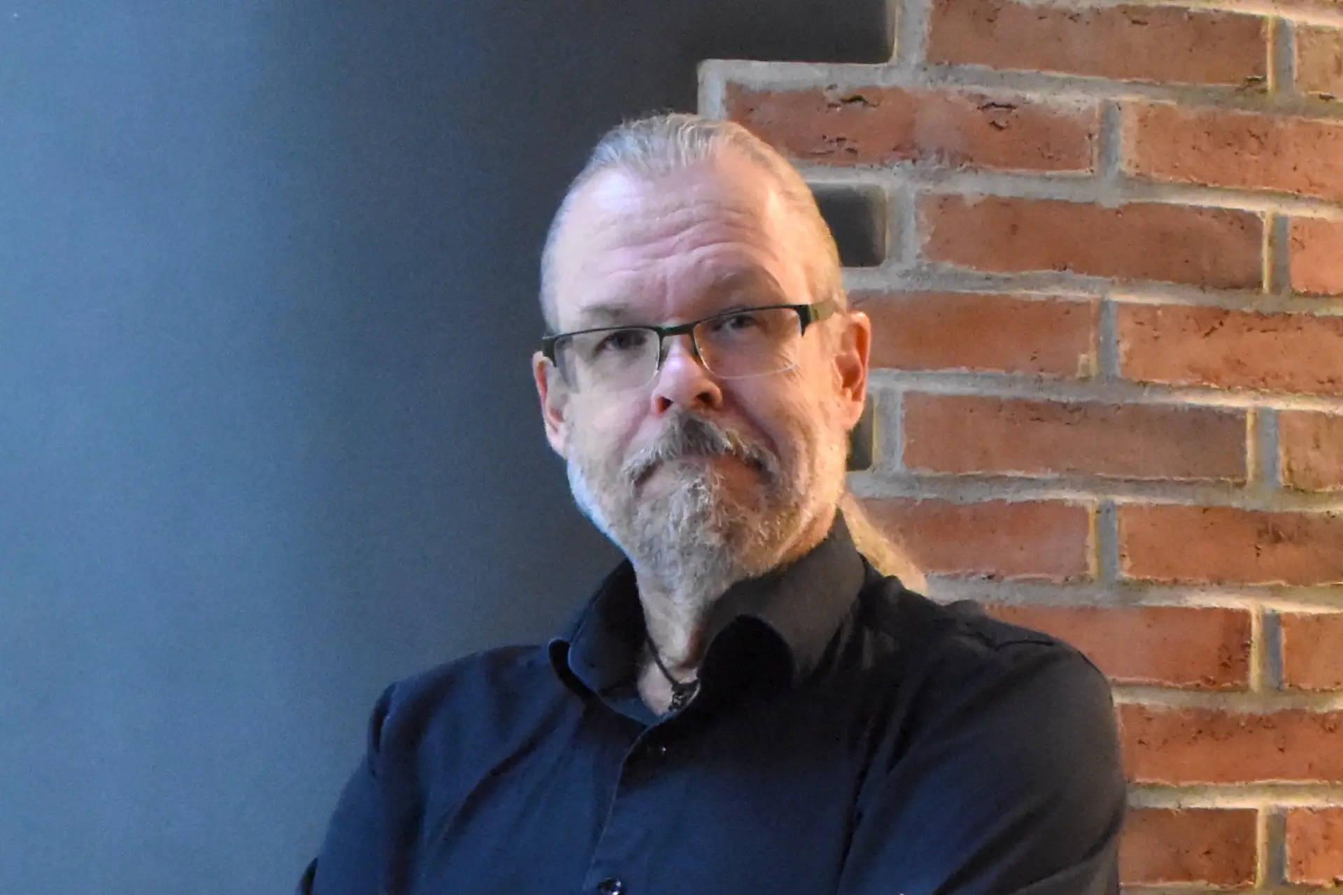 Kirjailija katsoo kameraan taustallaan harmaa seinä ja tiiliseinä