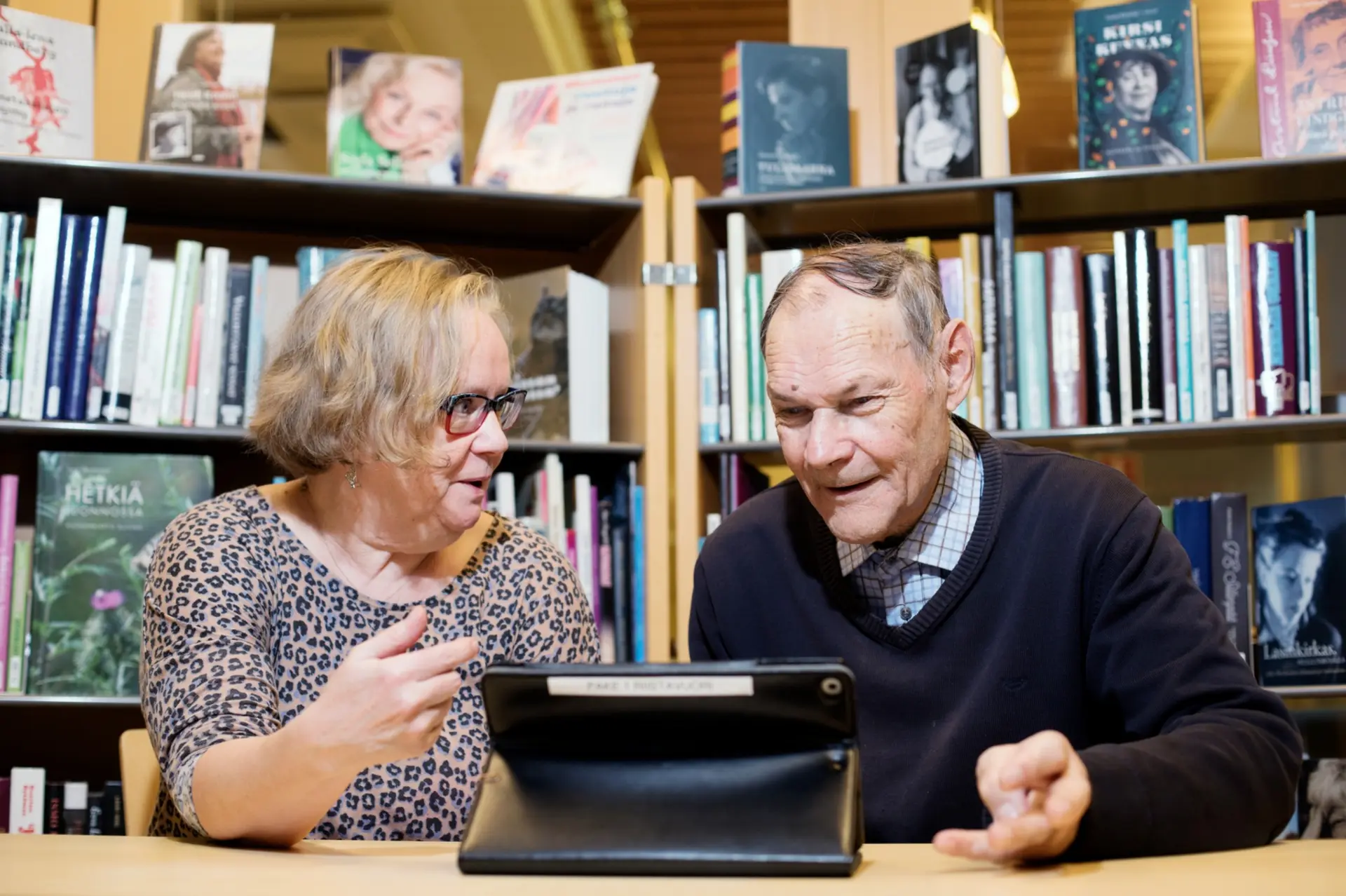 Seniori-ikäinen nainen auttaa seniori-ikäistä miestä digiasioissa.