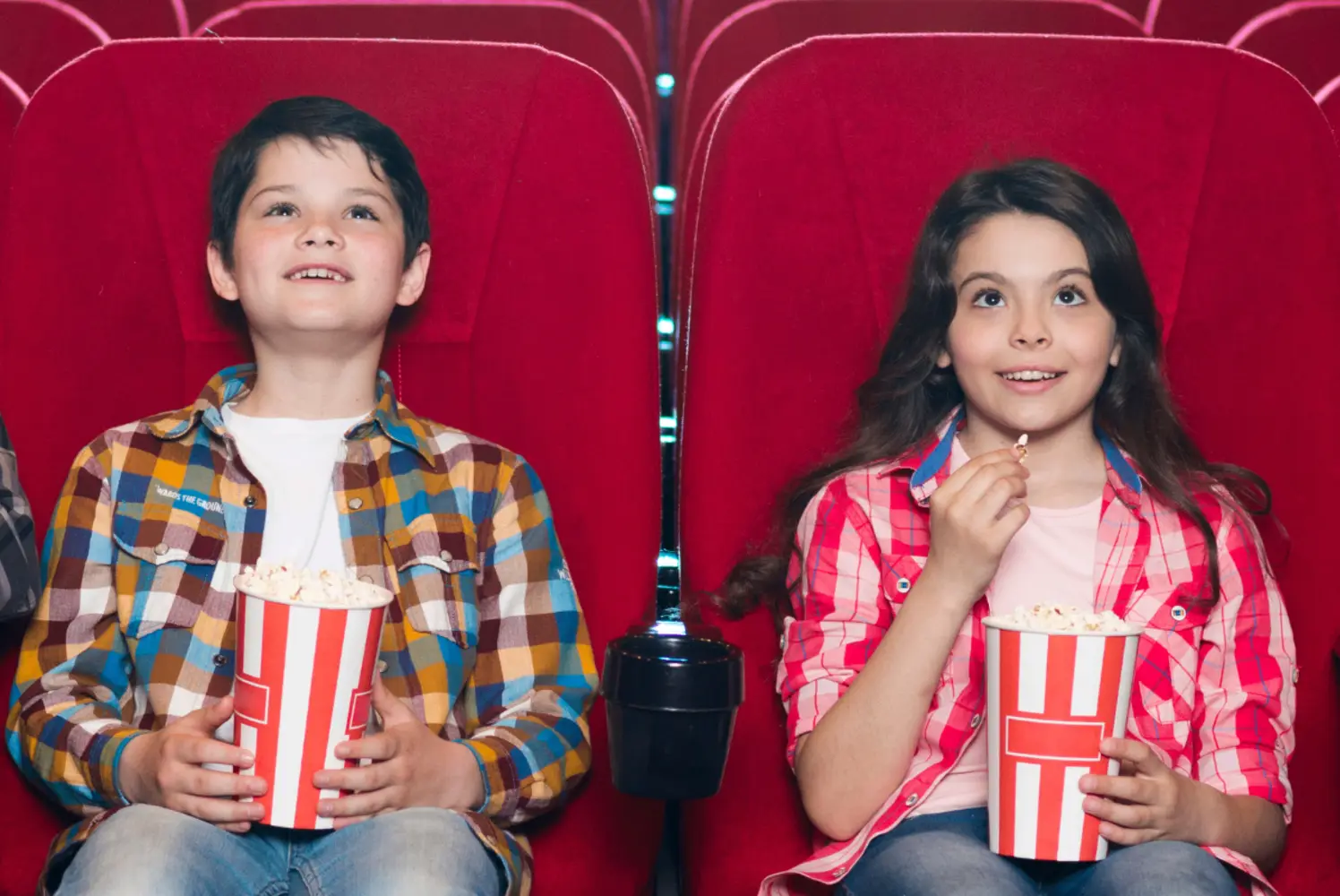 Kaksi lasta istuu elokuvateatterin katsomossa ja syö popcornia