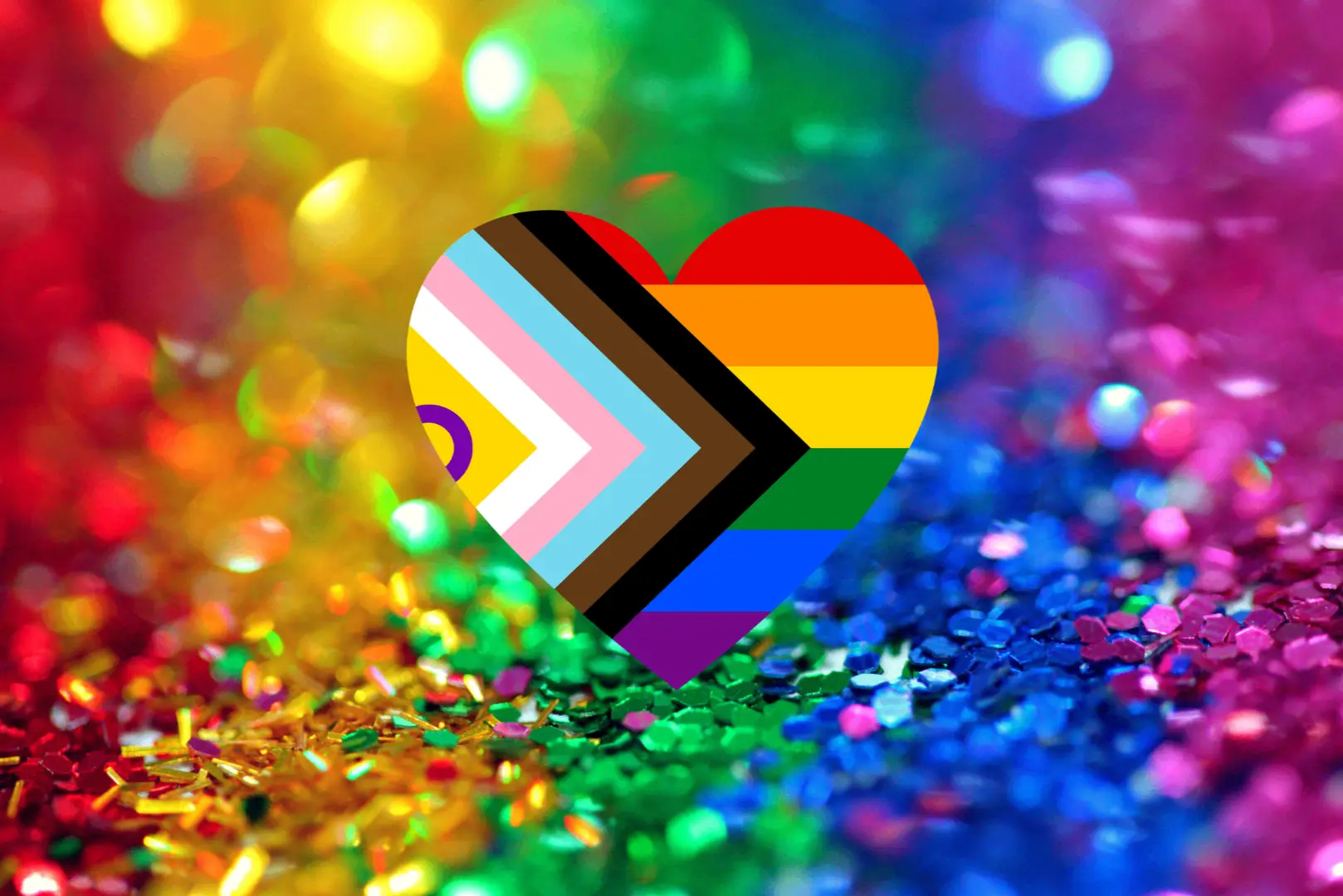 Keskellä sydämen muotoinen pridelippu ja taustalla glitteriä sateenkaaren väreissä.