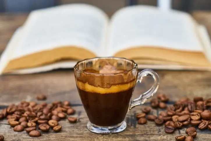 Coffee beans and a cup of coffee in front of an open book.