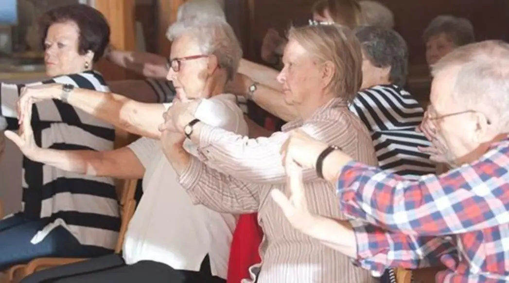 Vanhuksia jumppaamassa. Venyttelevät käsiä tuolilla istuen.