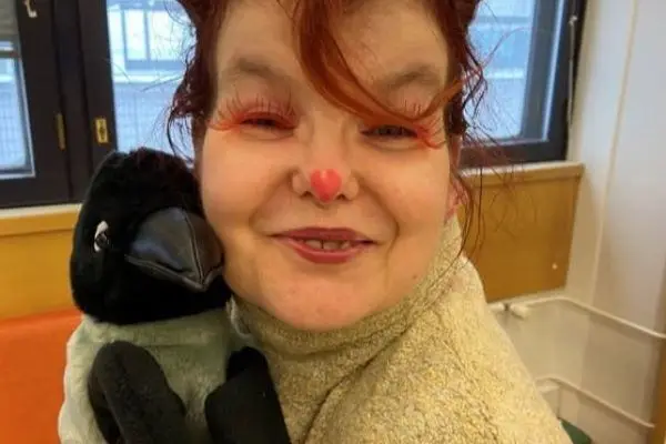 nainen hymyilee varispehmolelun vieressä
